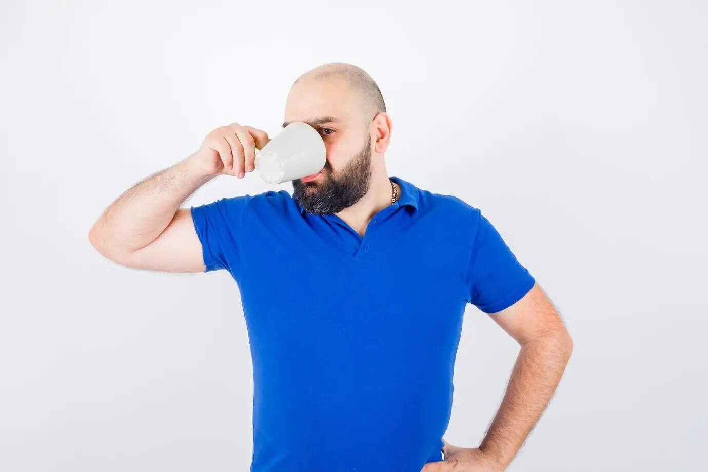 Молодой мужчина в синей рубашке пьёт, вид спереди.